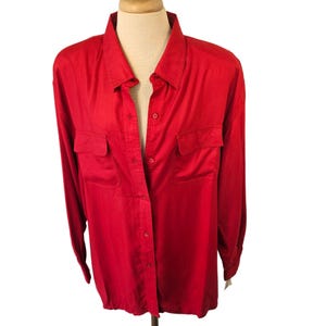 May include: A bright red button-down shirt with long sleeves and two chest pockets. The shirt is displayed on a mannequin and has a classic collar. The fabric appears to be smooth and slightly shiny.