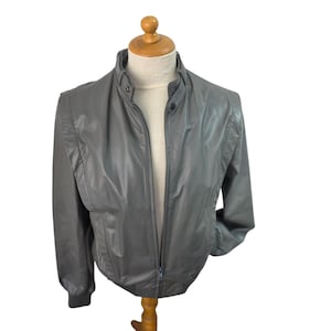 May include: A gray jacket with a high collar and a full-length zipper. The jacket is displayed on a mannequin and has a ribbed cuff and hem. The jacket appears to be made of a lightweight material.