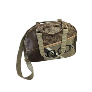 May include: A brown and tan leather duffel bag with a black and white logo that says "Volcom". The bag has a long shoulder strap and two top handles.