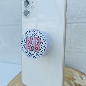 May include: White phone case with a black and white dalmatian print phone grip. The grip has the initials "KB" in pink.