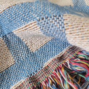 May include: A blue and white woven throw blanket with a colorful fringe. The blanket has a checkered pattern.