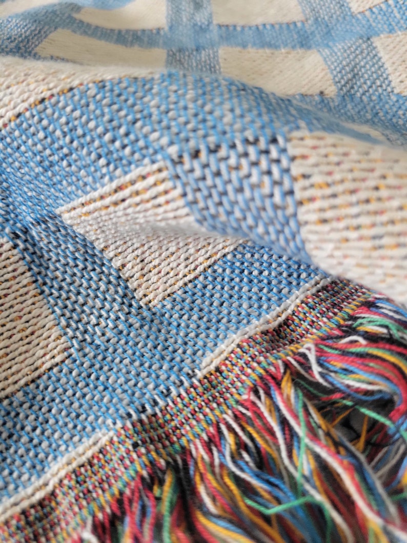 May include: A blue and white woven throw blanket with a colorful fringe. The blanket has a checkered pattern.