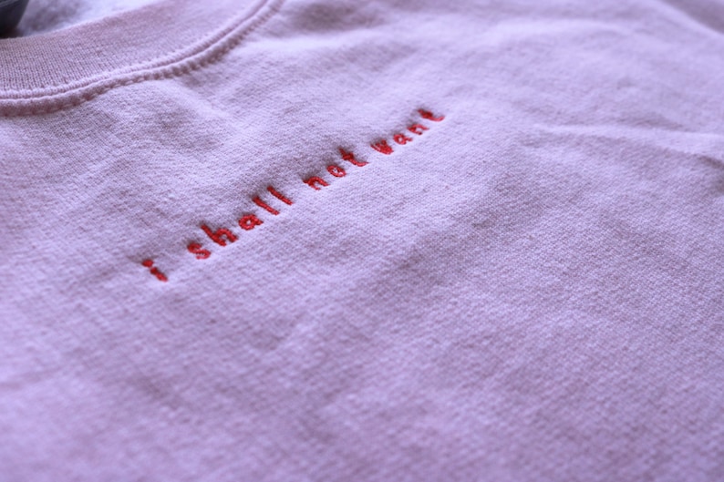 May include: A light pink sweatshirt with the phrase "I shall not want" embroidered in red thread.