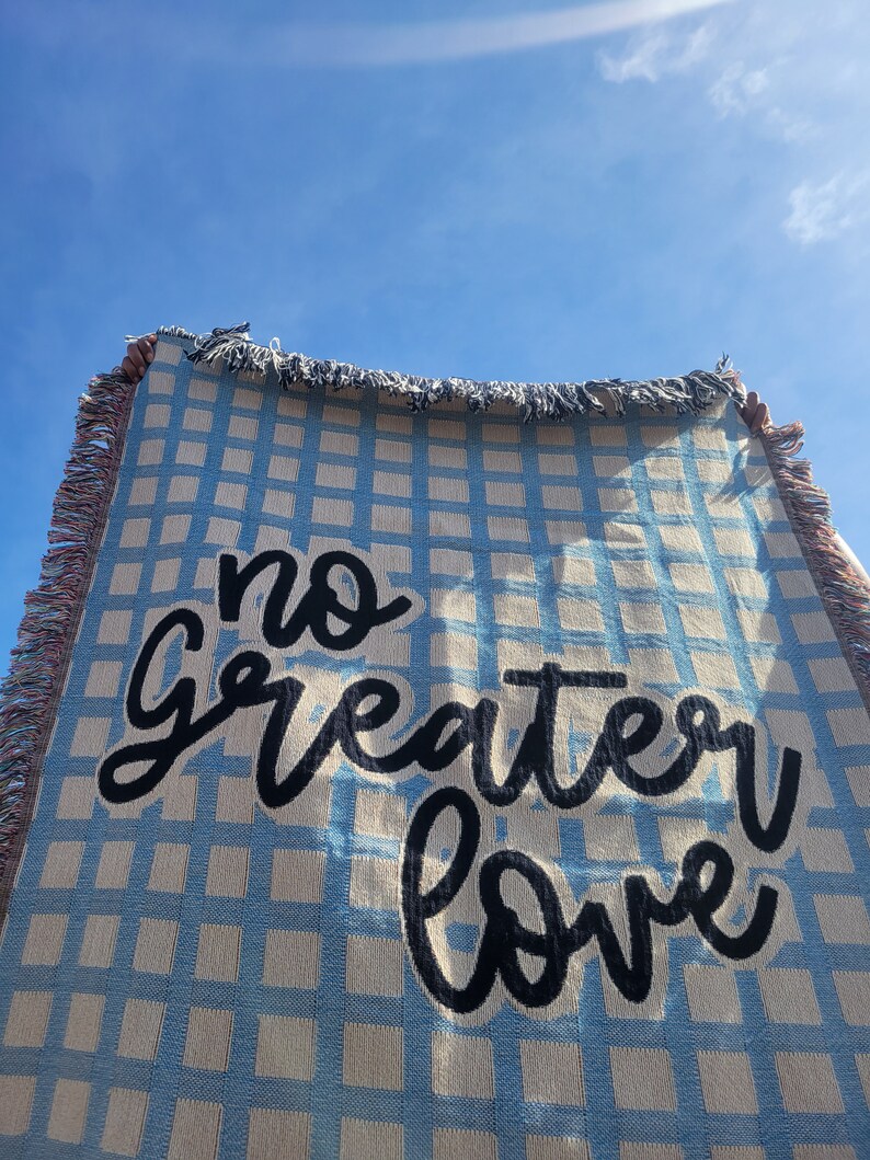 May include: A blue and white checkered woven throw blanket with the text "no greater love" in black cursive lettering.