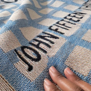 May include: A blue and white woven throw blanket with the text "JOHNNY FIFTEEN" woven into the fabric.