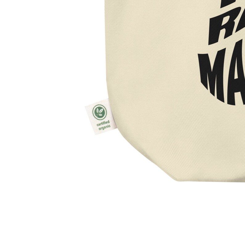 Op de afbeelding: Een beige tote bag met een zwarte cirkelvormige afbeelding met de tekst "Eat, Sleep, Race, Repeat". De tas heeft een groen label met de tekst "gecertificeerd biologisch".