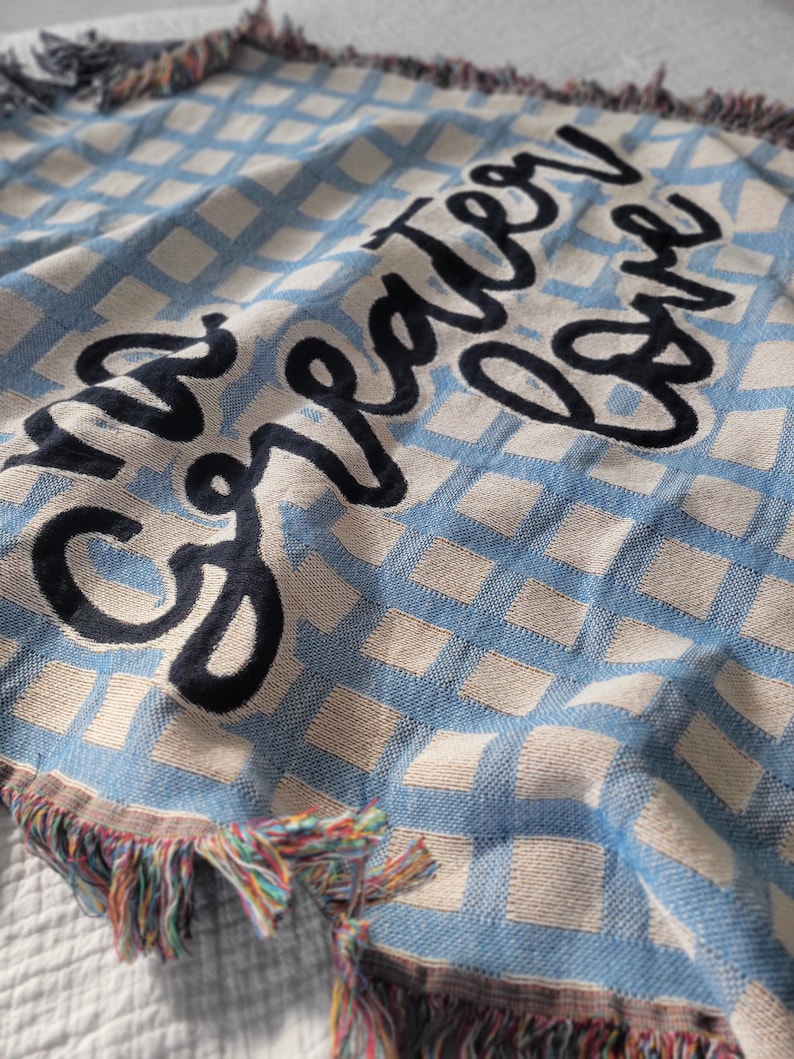May include: A blue and white woven throw blanket with the text "The greater love" embroidered in black.