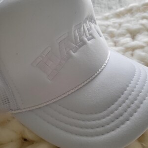 Puede incluir: Gorra de camionero blanca con un logotipo bordado en blanco que dice "WACKY" en una fuente en negrita de estilo 3D.