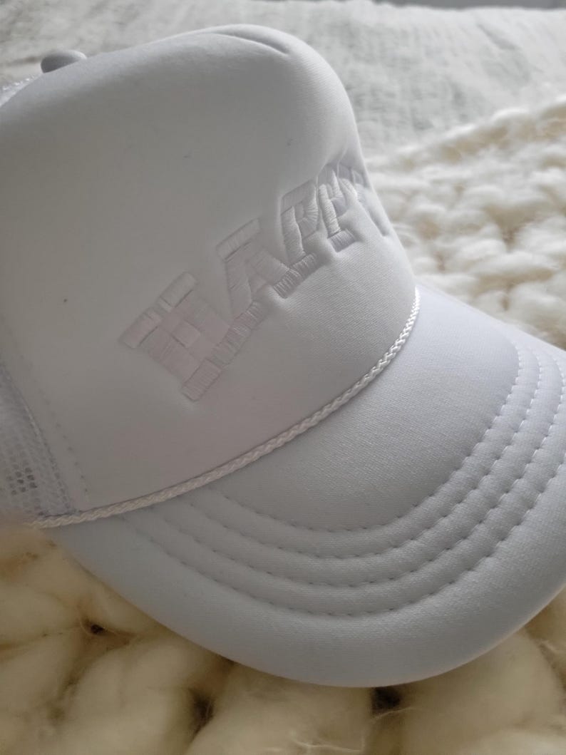 Puede incluir: Gorra de camionero blanca con un logotipo bordado en blanco que dice "WACKY" en una fuente en negrita de estilo 3D.