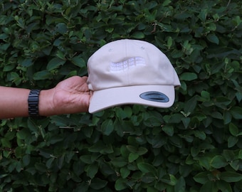 May include: A beige baseball cap with the text "Inspired by the world" repeated three times in white embroidery.
