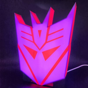 May include: A purple and red 3D printed lamp shaped like the Decepticon symbol from the Transformers franchise.
