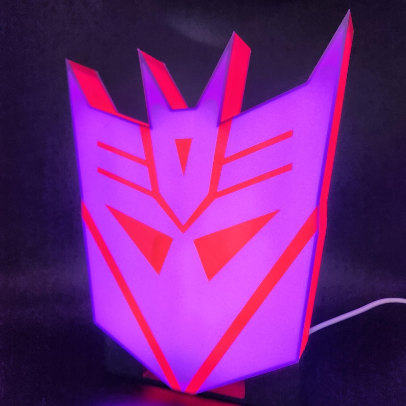 May include: A purple and red 3D printed lamp shaped like the Decepticon symbol from the Transformers franchise.