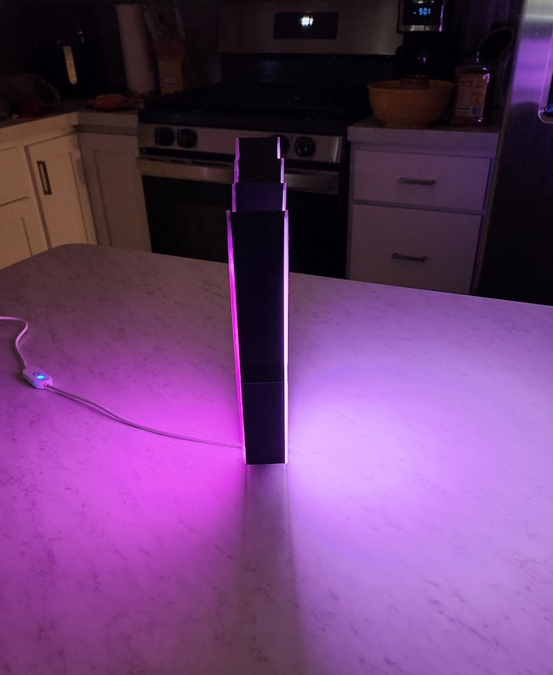 May include: A black, rectangular lamp with a pink light emanating from the sides. The lamp is sitting on a white countertop.
