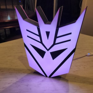 May include: A purple and black 3D printed light shaped like the Decepticon symbol from the Transformers franchise.
