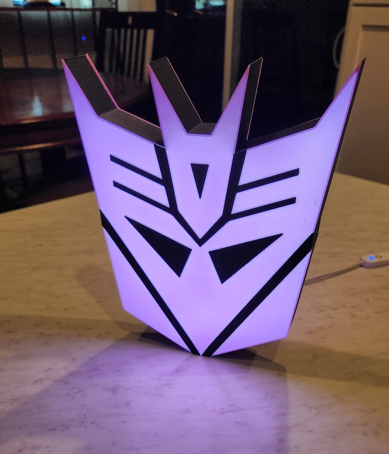 May include: A purple and black 3D printed light shaped like the Decepticon symbol from the Transformers franchise.