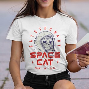 May include: White t-shirt with a graphic of a cat wearing an astronaut helmet. The graphic says "Cats-tronaut Space Cat Meow on Mars".