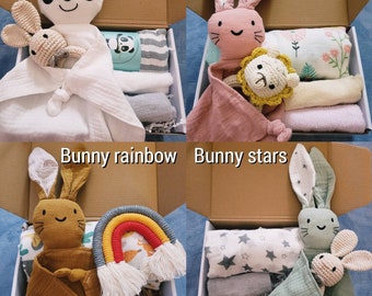 May include: Four gift boxes with different baby themes. The boxes contain a plush toy, a muslin blanket, and a small toy. The themes are Panda, Pink bunny, Bunny rainbow, and Bunny stars.