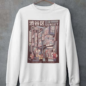 May include: White sweatshirt with a graphic print of a city street scene at sunset. The graphic features a Japanese cityscape with neon signs and people walking. The text "渋谷区日没 SUNSET" is printed above the graphic. The text "SOUND OF CITY VIBES" is printed below the graphic.