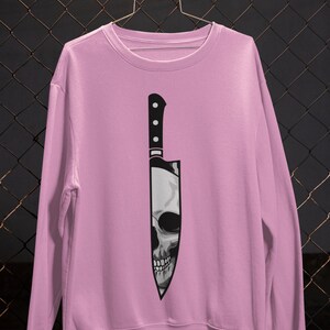 May include: A pink sweatshirt with a graphic of a black knife with a skull inside.