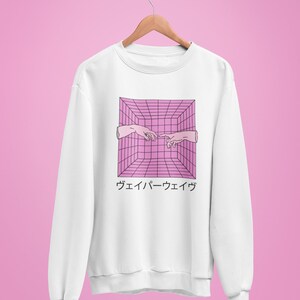May include: White sweatshirt with a pink and black geometric design featuring two hands reaching towards each other. Japanese text is below the graphic. The sweatshirt is hanging on a wooden hanger against a pink background.