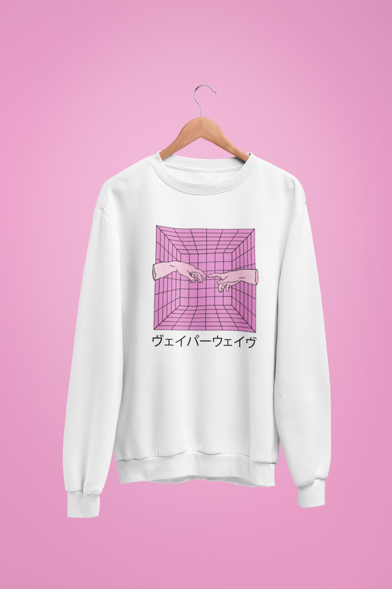 May include: White sweatshirt with a pink and black geometric design featuring two hands reaching towards each other. Japanese text is below the graphic. The sweatshirt is hanging on a wooden hanger against a pink background.