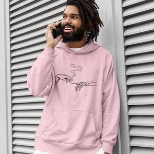 May include: A pink hoodie with a black and white graphic print of two hands, one human and one skeletal, passing a cigarette. The graphic is a parody of Michelangelo's The Creation of Adam.