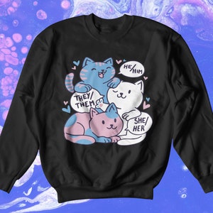 May include: Black sweatshirt with a graphic of three cats stacked on top of each other. The cats are wearing different colored collars and have speech bubbles above their heads. The speech bubbles say "They/Them", "He/Him", and "She/Her".