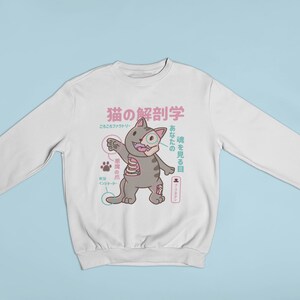 May include: White sweatshirt featuring a cartoon cat illustration. The cat is grey with pink accents and has a skeleton inside. The text on the sweatshirt is in Japanese and reads "Cat Anatomy".