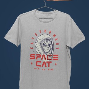 May include: A gray t-shirt with a graphic of a cat wearing an astronaut helmet. The text on the shirt reads "Catstronaut Space Cat Meow On Mars".