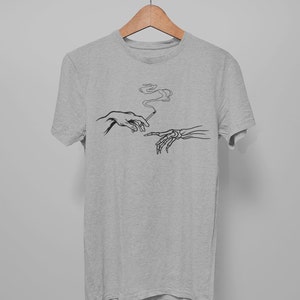 May include: A heather grey t-shirt with a black and white graphic of two hands reaching towards each other, one human and one skeletal, passing a cigarette.