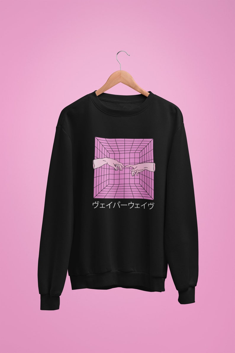 May include: Black sweatshirt featuring a pink and white graphic of two hands reaching towards each other within a 3D grid. Japanese text is below the graphic. The sweatshirt is hanging on a wooden hanger against a pink background.