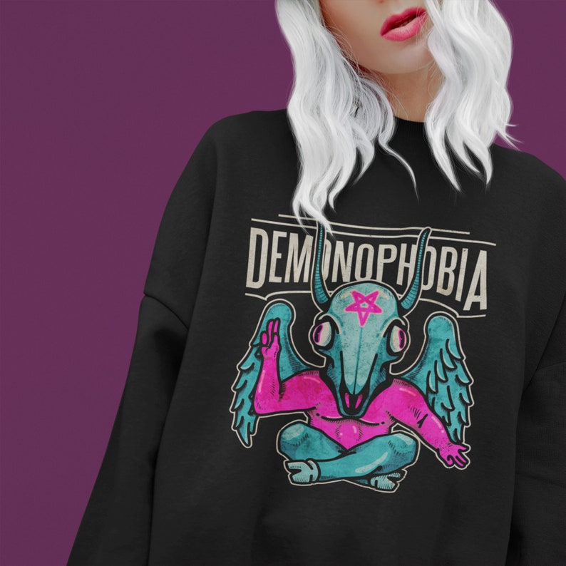 May include: Black sweatshirt with a graphic of a blue demon with pink wings and a pentagram on its head. The text "DEMONOPHOBIA" is printed in white above the demon.