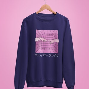 May include: Navy blue sweatshirt featuring a pink geometric design with two hands nearly touching, and Japanese text below. The design is reminiscent of the Creation of Adam. The sweatshirt is hanging on a wooden hanger against a pink background.