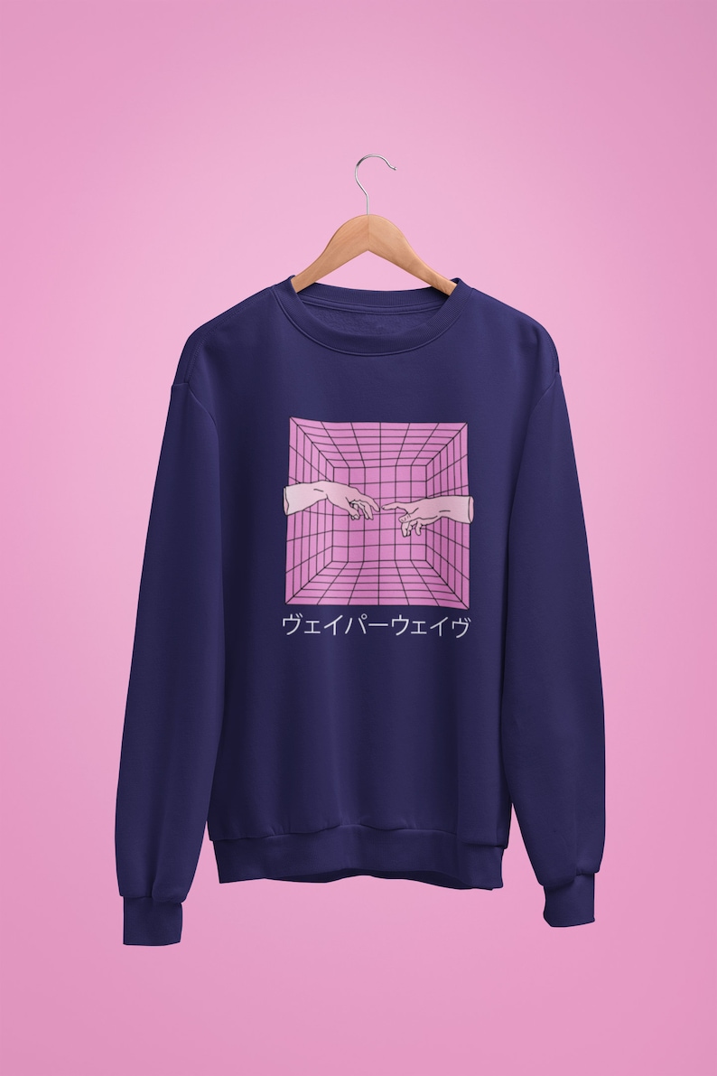 May include: Navy blue sweatshirt featuring a pink geometric design with two hands nearly touching, and Japanese text below. The design is reminiscent of the Creation of Adam. The sweatshirt is hanging on a wooden hanger against a pink background.