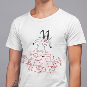 Peut inclure: T-shirt blanc avec une illustration noire et rouge d'une ch&egrave;vre avec des cornes et un pentagramme sur le front, courant sur un jeu de marelle rouge et noir avec des flammes sur les c&ocirc;t&eacute;s. Les chiffres 1, 5 et 9 sont visibles sur le jeu.