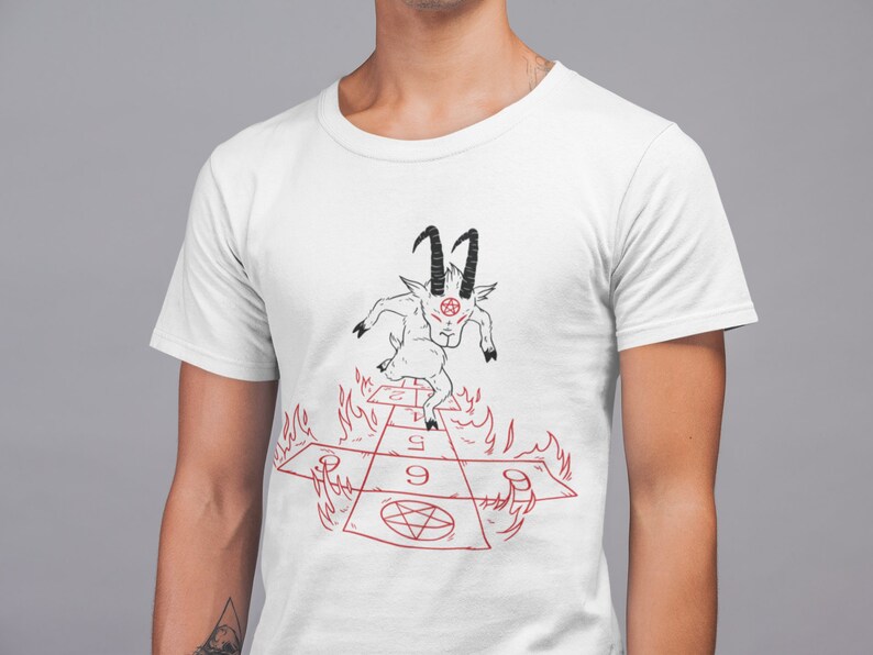 Peut inclure: T-shirt blanc avec une illustration noire et rouge d'une ch&egrave;vre avec des cornes et un pentagramme sur le front, courant sur un jeu de marelle rouge et noir avec des flammes sur les c&ocirc;t&eacute;s. Les chiffres 1, 5 et 9 sont visibles sur le jeu.