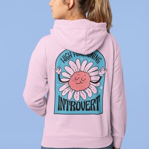 May include: A pink hoodie with a blue and white graphic on the back. The graphic features a cartoon daisy with a face and the text "High Functioning Introvert".