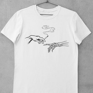 May include: White t-shirt with a black line drawing of two hands, one human and one skeletal, passing a cigarette. The cigarette is smoking.