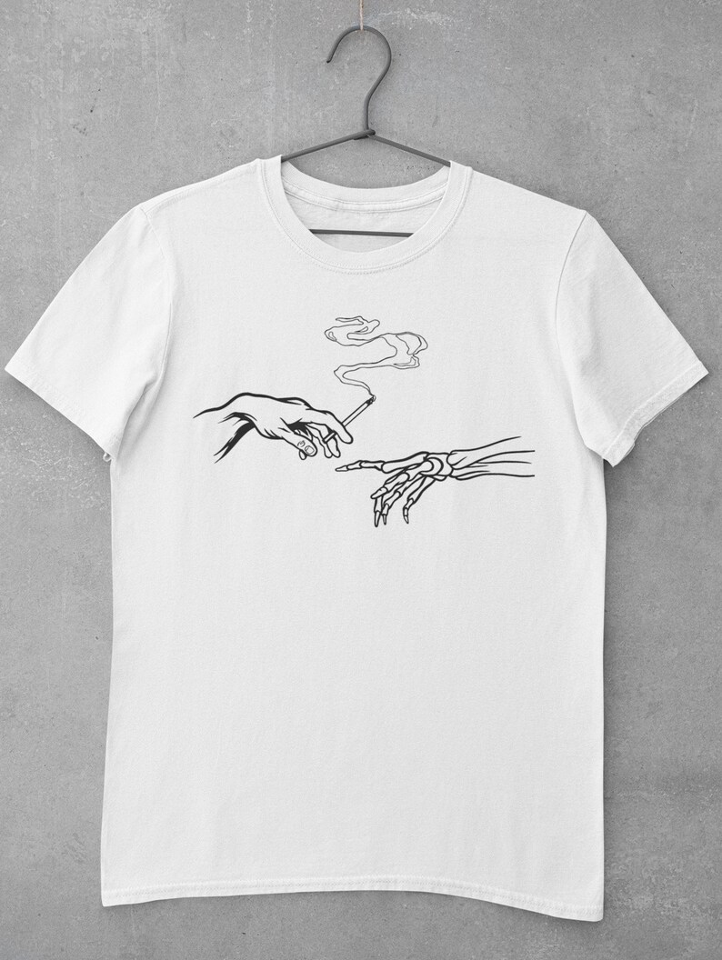 May include: White t-shirt with a black line drawing of two hands, one human and one skeletal, passing a cigarette. The cigarette is smoking.