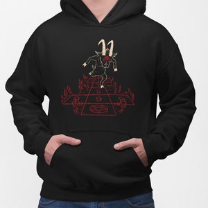 Peut inclure: Sweat-shirt &agrave; capuche noir avec un motif repr&eacute;sentant un bouc noir aux yeux rouges et aux cornes courant sur un jeu de marelle rouge et ardent avec un pentagramme au centre.