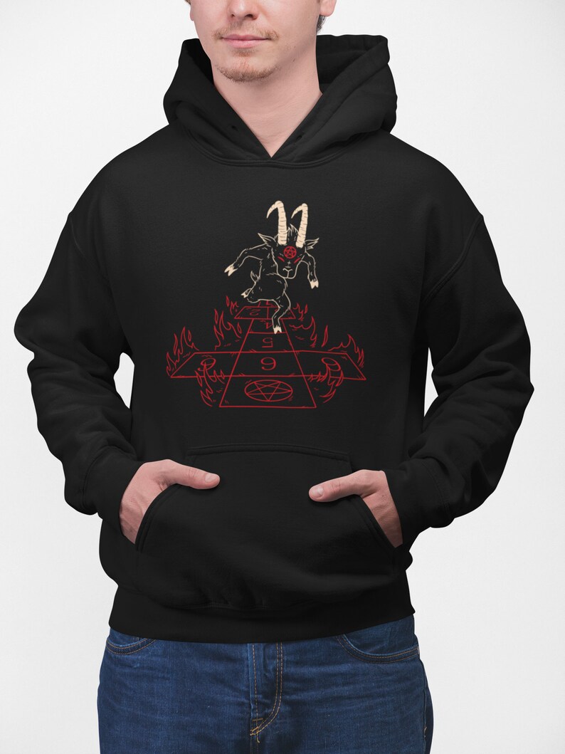 Peut inclure: Sweat-shirt &agrave; capuche noir avec un motif repr&eacute;sentant un bouc noir aux yeux rouges et aux cornes courant sur un jeu de marelle rouge et ardent avec un pentagramme au centre.