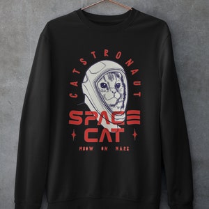 May include: Black sweatshirt with a white and red graphic of a cat wearing an astronaut helmet. The text reads "Catstronaut Space Cat Meow On Mars".