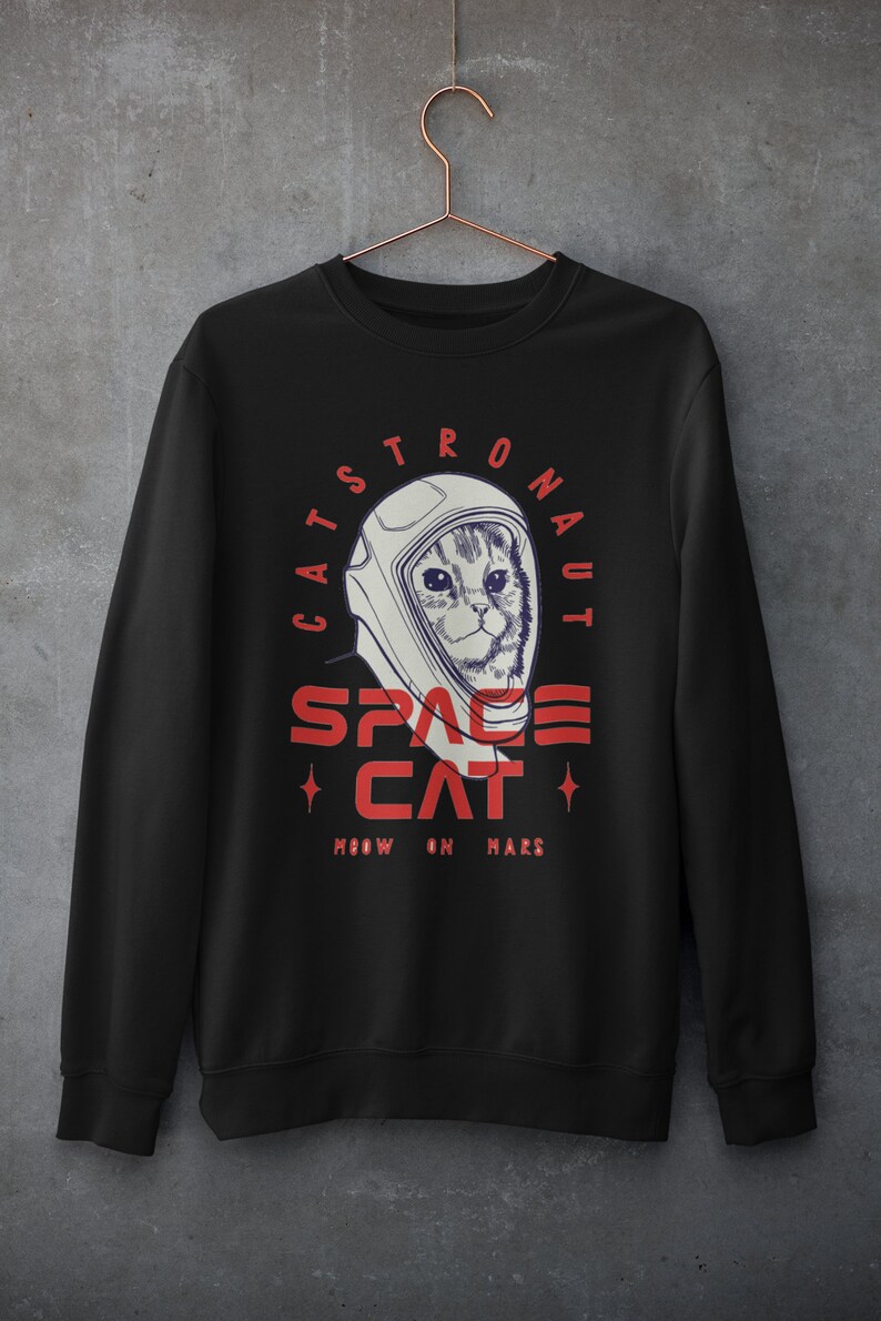 May include: Black sweatshirt with a white and red graphic of a cat wearing an astronaut helmet. The text reads "Catstronaut Space Cat Meow On Mars".