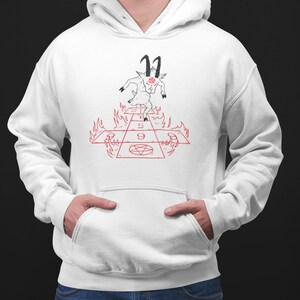 Peut inclure: Sweat-shirt &agrave; capuche blanc avec une illustration en noir et blanc d'une ch&egrave;vre avec des cornes et un pentagramme sur le front. La ch&egrave;vre se tient sur un damier rouge et blanc avec des flammes sur les c&ocirc;t&eacute;s. Le damier porte les chiffres 1, 5 et 9.