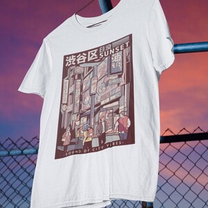 May include: White t-shirt with a graphic print of a city street scene at sunset. The graphic features buildings with Japanese text and the words "Sunset" and "Sound of City Vibes".