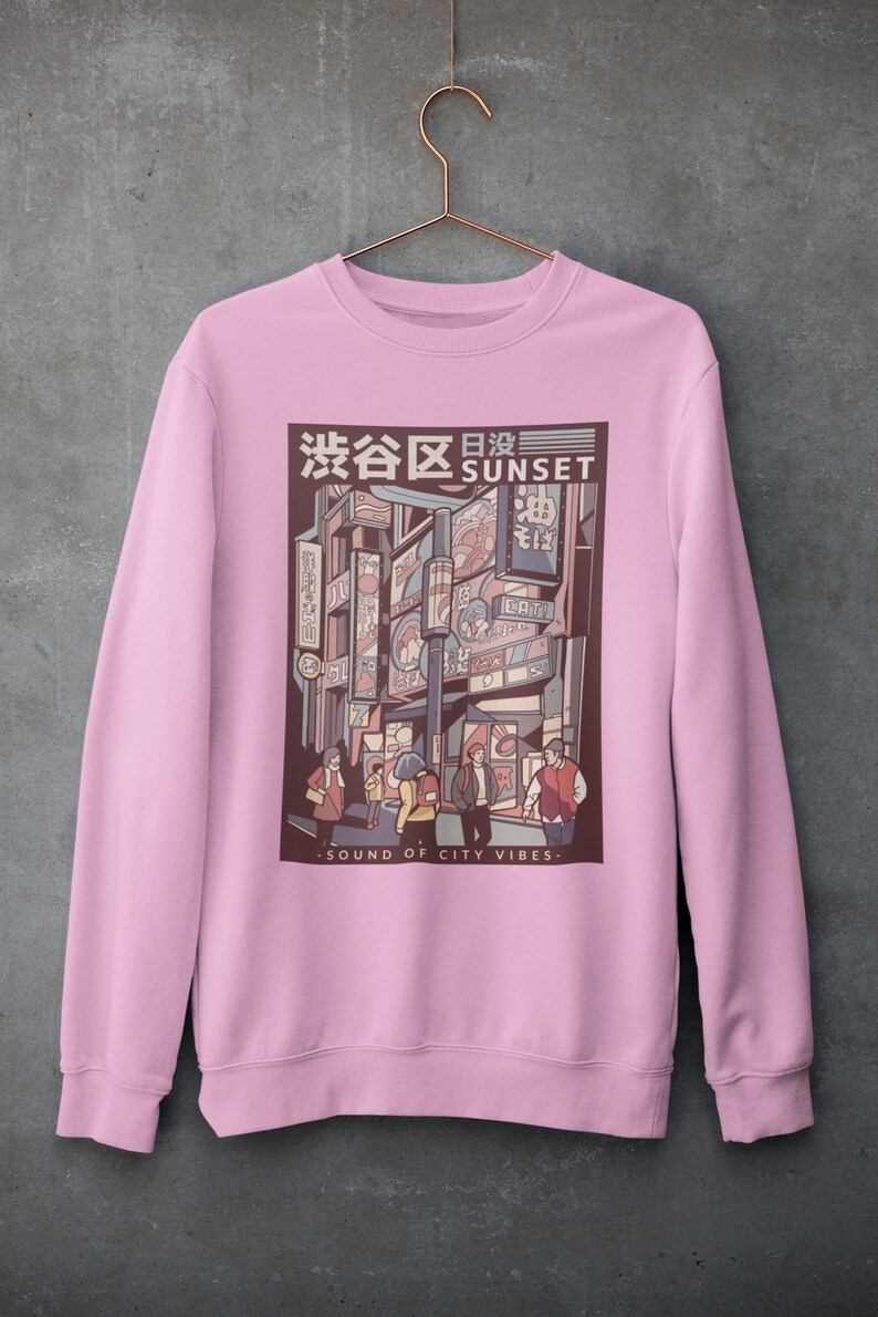 May include: Pink sweatshirt with a graphic print of a city street scene at sunset. The graphic features a Japanese cityscape with neon signs and people walking. The text "渋谷日没 SUNSET" is printed above the graphic. The text "SOUND OF CITY VIBES" is printed below the graphic.