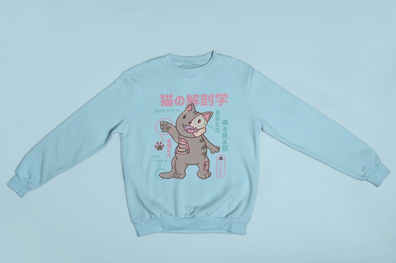 May include: A light blue sweatshirt featuring a cartoon cat anatomy illustration. The cat is labelled in Japanese with the text "猫の解剖学", which translates to "Cat Anatomy".