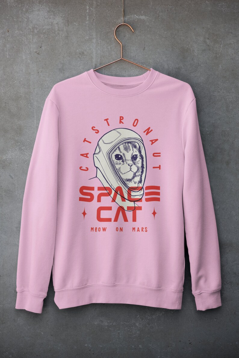 May include: Pink sweatshirt with a graphic of a cat wearing an astronaut helmet. The text reads "Catstronaut Space Cat Meow On Mars".