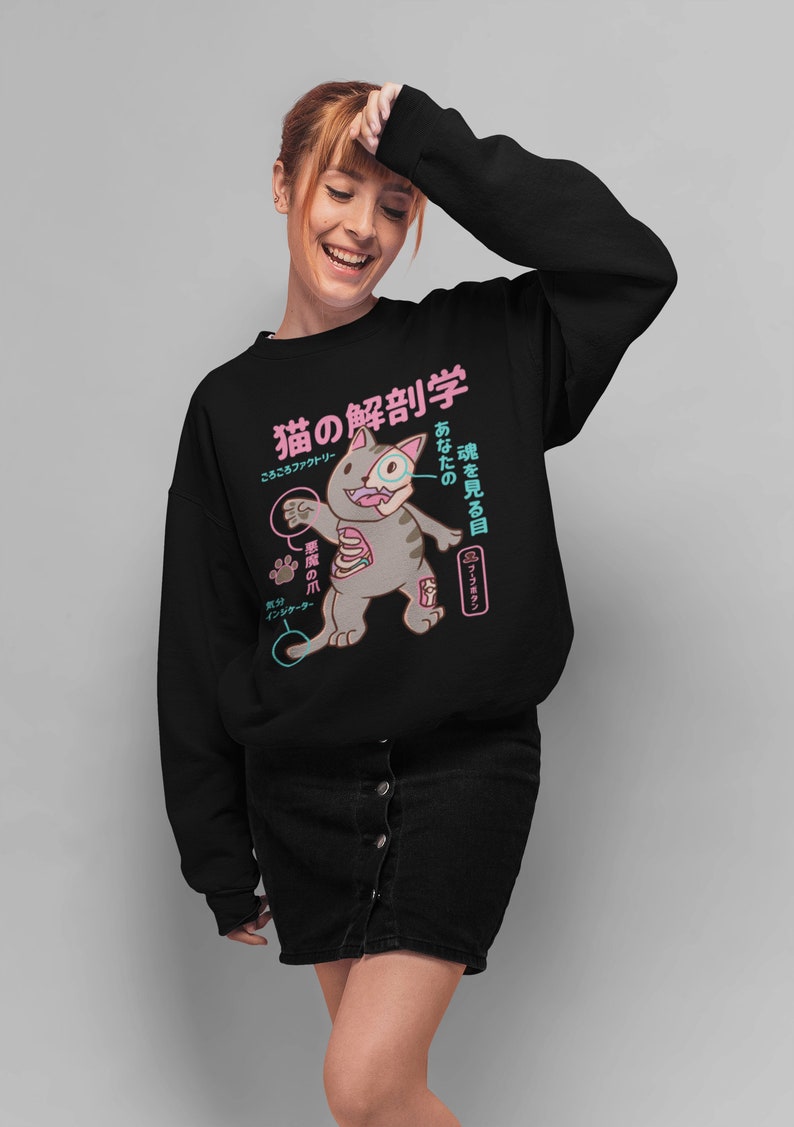 May include: Black sweatshirt featuring a cartoon cat with anatomical details labelled in Japanese. The text reads "猫の解剖学", which translates to "Cat Anatomy", and "あなたの魂を見る目", which translates to "The eye that sees your soul".