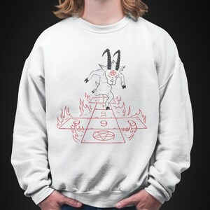 Peut inclure: Sweat-shirt blanc avec un motif noir et rouge d'une ch&egrave;vre avec des cornes et un pentagramme sur le front, marchant sur un jeu de marelle enflamm&eacute; avec les chiffres 1, 2, 3, 4, 5, 6, 7, 8 et 9.